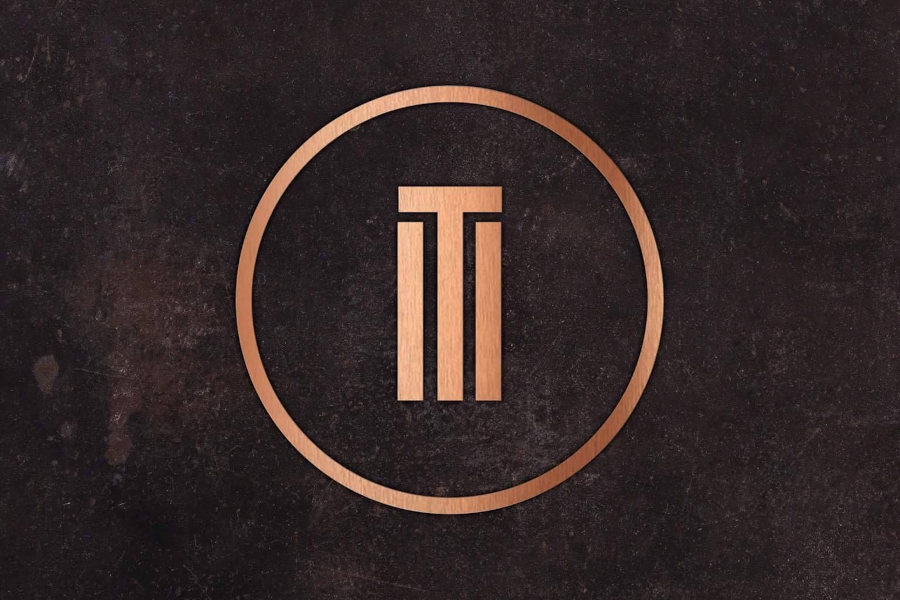 Circular Trademark Bar logo with geometric lTl symbol in copper tone centred on a dark textured surface.