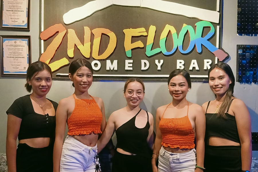 Five women standing together inside 2nd Floor Comedy Bar in Davao with branded wall sign and casual nightlife atmosphere.